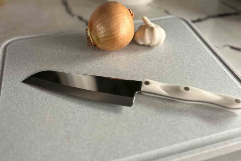 japanese style knife on cutting board with onion and garlic